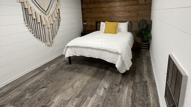 A bedroom with a wooden headboard, a white bedspread, and a decorative wall hanging. - Comfy, Clean & Pet Friendly (Gonzales)
