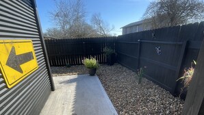 A concrete patio with a black metal fence, a yellow directional sign, and a potted plant. - Comfy, Clean & Pet Friendly (Gonzales)