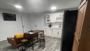 A compact kitchen with white cabinets, a black refrigerator, and a dining area with a brown sofa and stools. - Comfy, Clean & Pet Friendly (Gonzales)