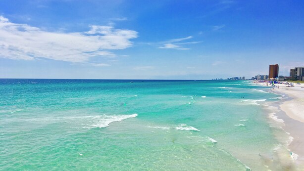 A beach with clear turquoise water, a sandy shore, and a city skyline in the background.