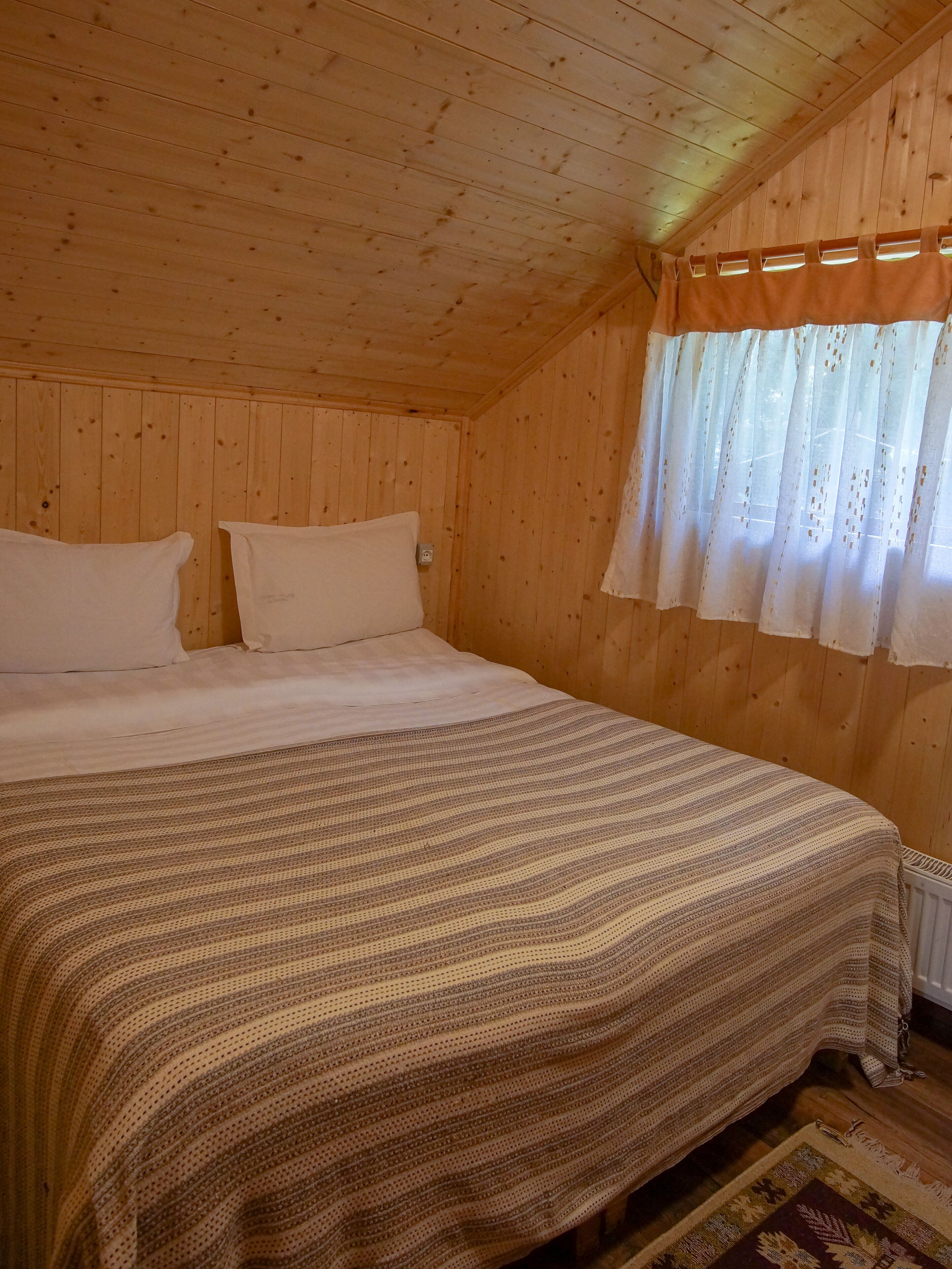Un dormitorio de cabaña de madera con cama, almohadas y una ventana con cortinas.