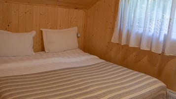 Un dormitorio de cabaña de madera con cama, almohadas y una ventana con cortinas.