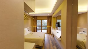 Une chambre d’hôtel comprenant un lit, une table de chevet, un miroir, une fenêtre avec des rideaux et un téléviseur.