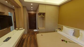 Una habitación de hotel moderna con suelo de madera, una cama con ropa blanca, un televisor sobre un mueble bajo y una mesita con un control remoto.