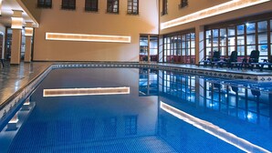 Une grande piscine intérieure avec un sol carrelé de bleu, des poutres en bois au plafond et une verrière.