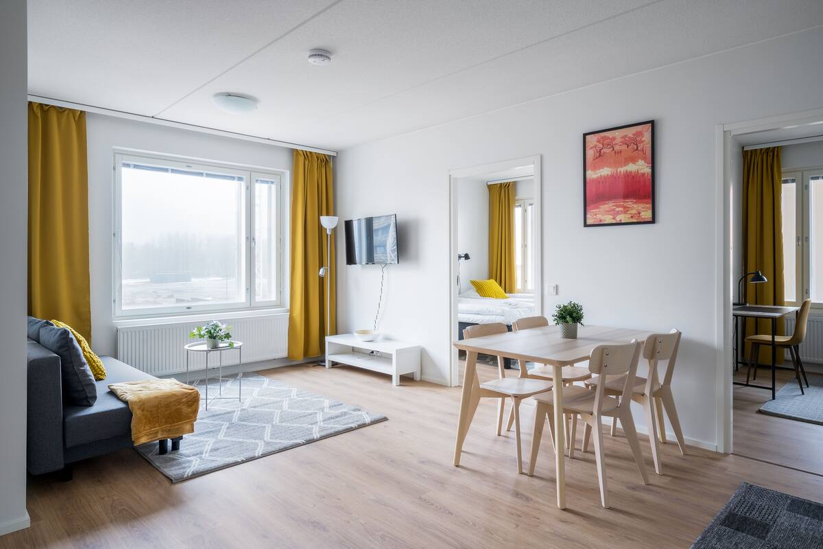 A modern living room with a sofa, a dining table with chairs, a TV, and a painting on the wall.