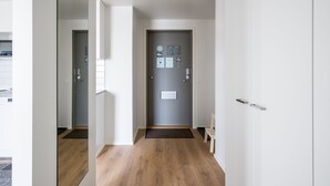 Un pasillo moderno con suelo de madera, una puerta gris con un tablón de anuncios y un pequeño banco.