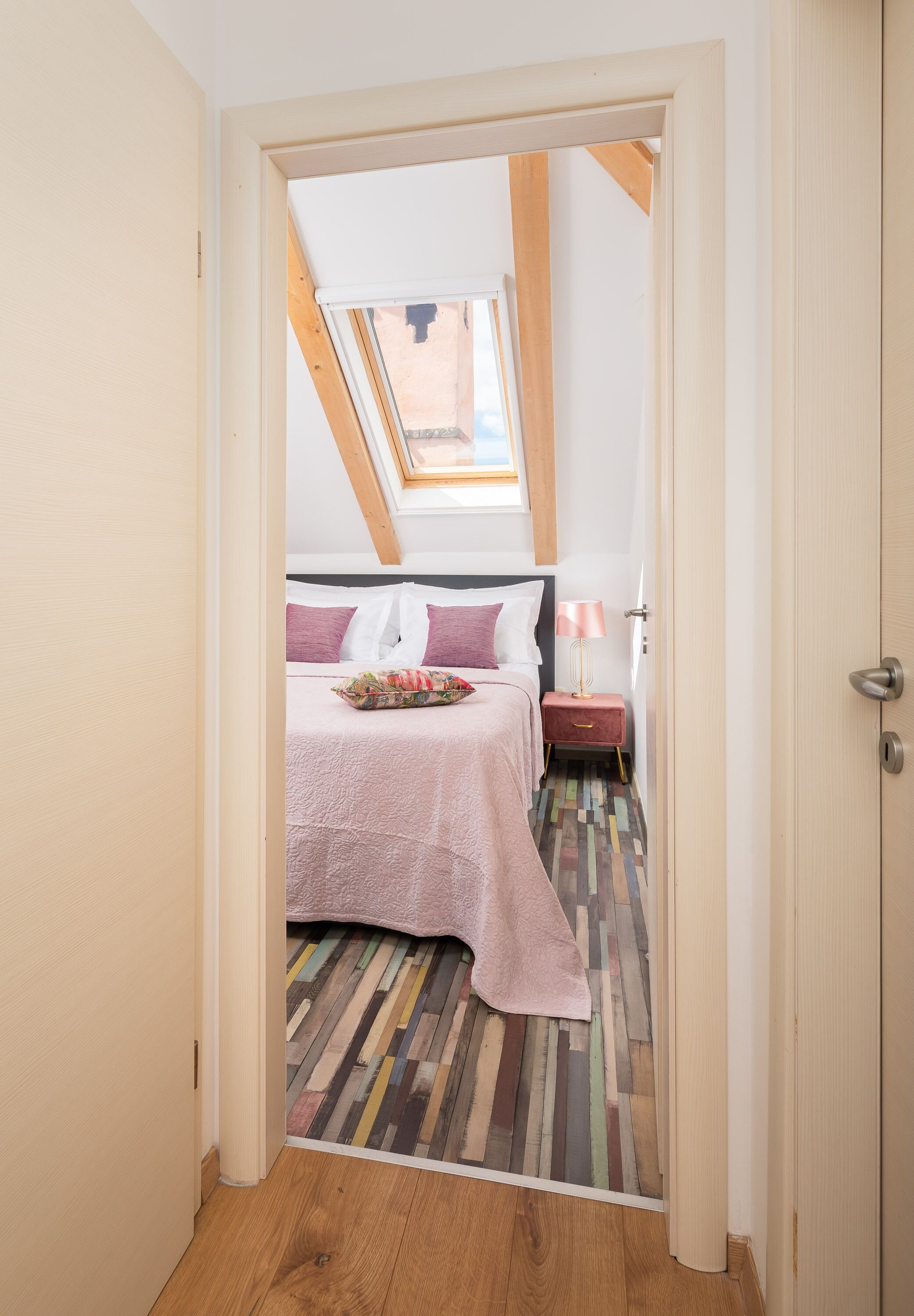 A narrow hallway leading to a bedroom with a sloped ceiling and a skylight.
