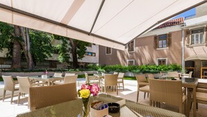 Un espace extérieur aménagé en terrasse, avec des meubles en osier, une table en verre et un vase rempli de fleurs.
