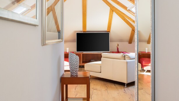 Une chambre de style loft moderne avec un plafond en pente, des poutres en bois, une grande télévision, un canapé et un fauteuil.