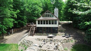 Eine zweistöckige Hütte mit einer Terrasse, umgeben von einem Wald.