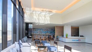 A modern hotel lobby with a reception desk, seating area, and a mural on the wall. - Fortune D Phitsanulok Hotel (Phitsanulok)