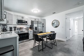 Een moderne keuken met roestvrijstalen apparatuur, een eettafel met stoelen en een grote spiegel aan de muur.