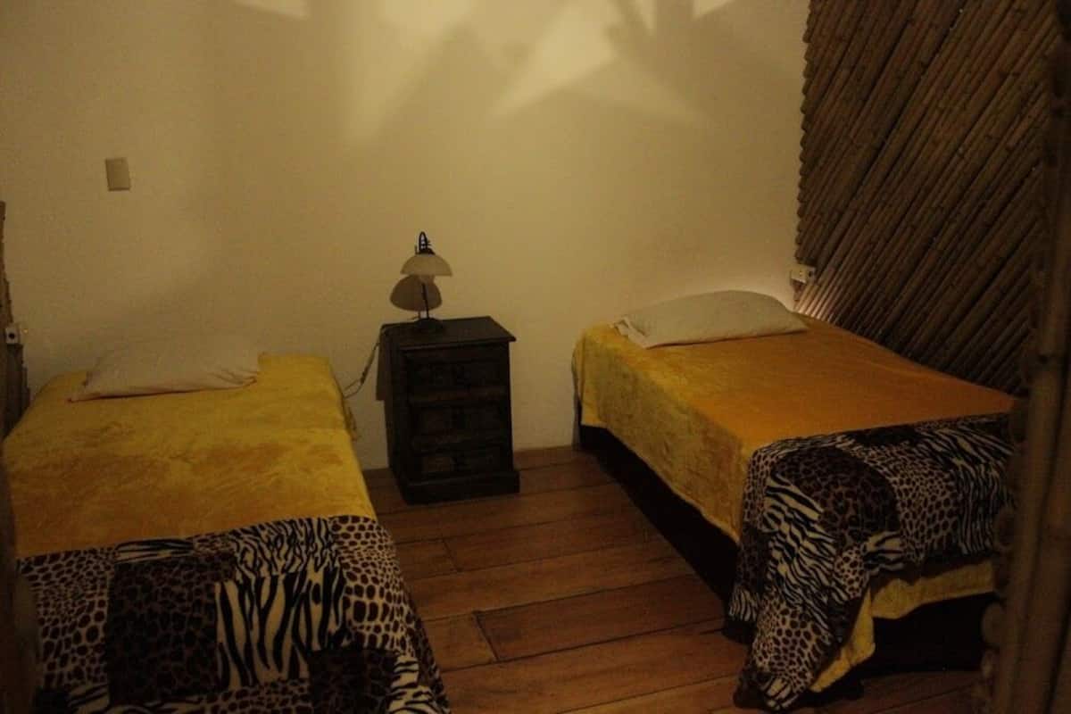 Une petite pièce avec deux lits simples, une table de chevet avec une lampe et un plancher en bois.