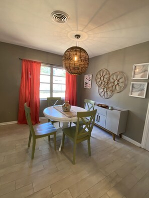 A dining area with a round table, green chairs, a hanging light fixture, and a window with red curtains. - Mid Century Bungalow in the heart of Lakeland.  Close to Leggo Land, (Lakeland)