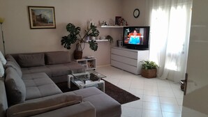 Ein Wohnzimmer mit einer Couch, einem Couchtisch, einem Fernseher und verschiedenen Pflanzen.
