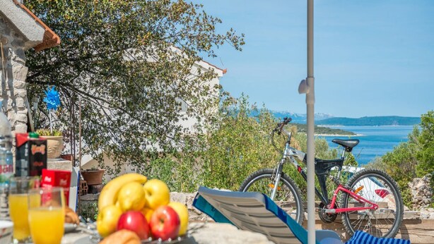Een tafel met fruit, een croissant en drankjes, een rode fiets en een prachtig uitzicht op zee en bergen.