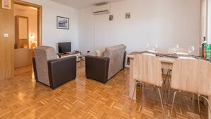 Een gemeubileerde woonkamer met een televisie, twee banken, een eettafel met stoelen en een houten parketvloer.