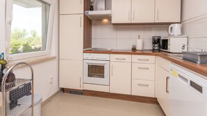 Een kleine keuken met witte kastjes, een fornuis, een magnetron en een vaatwasser.