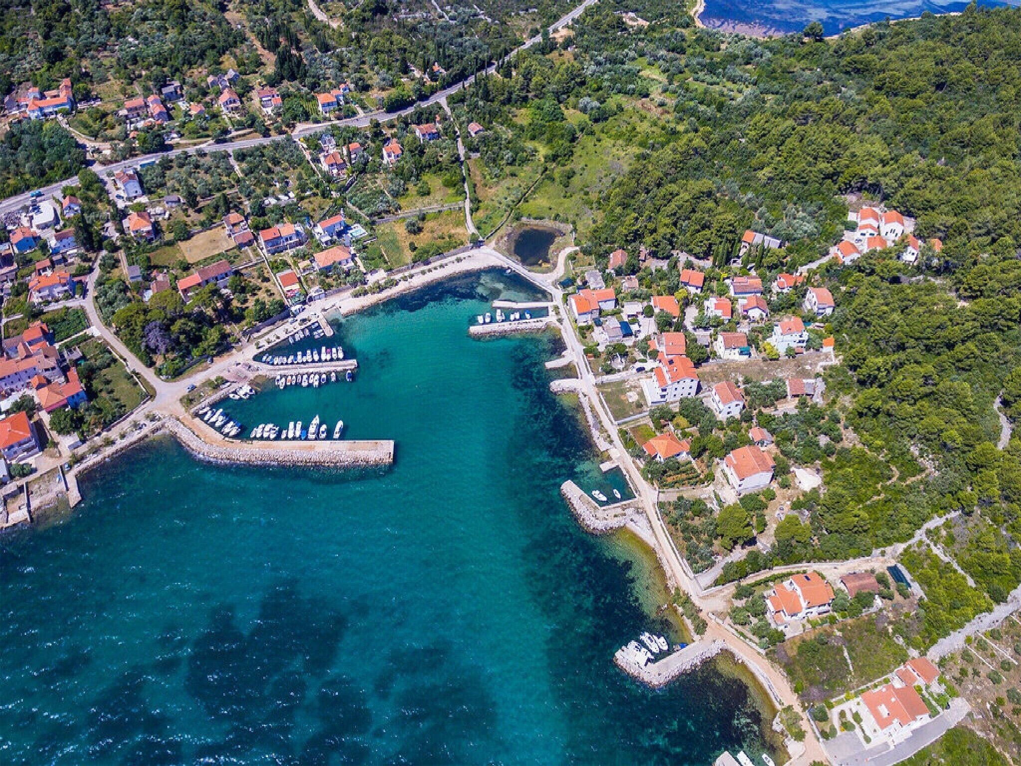 An aerial view of a coastal town with residential buildings, a marina, and a clear blue harbor.