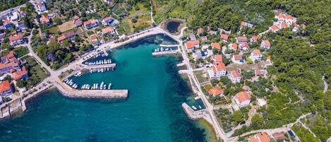 An aerial view of a coastal town with residential buildings, a marina, and a clear blue harbor.
