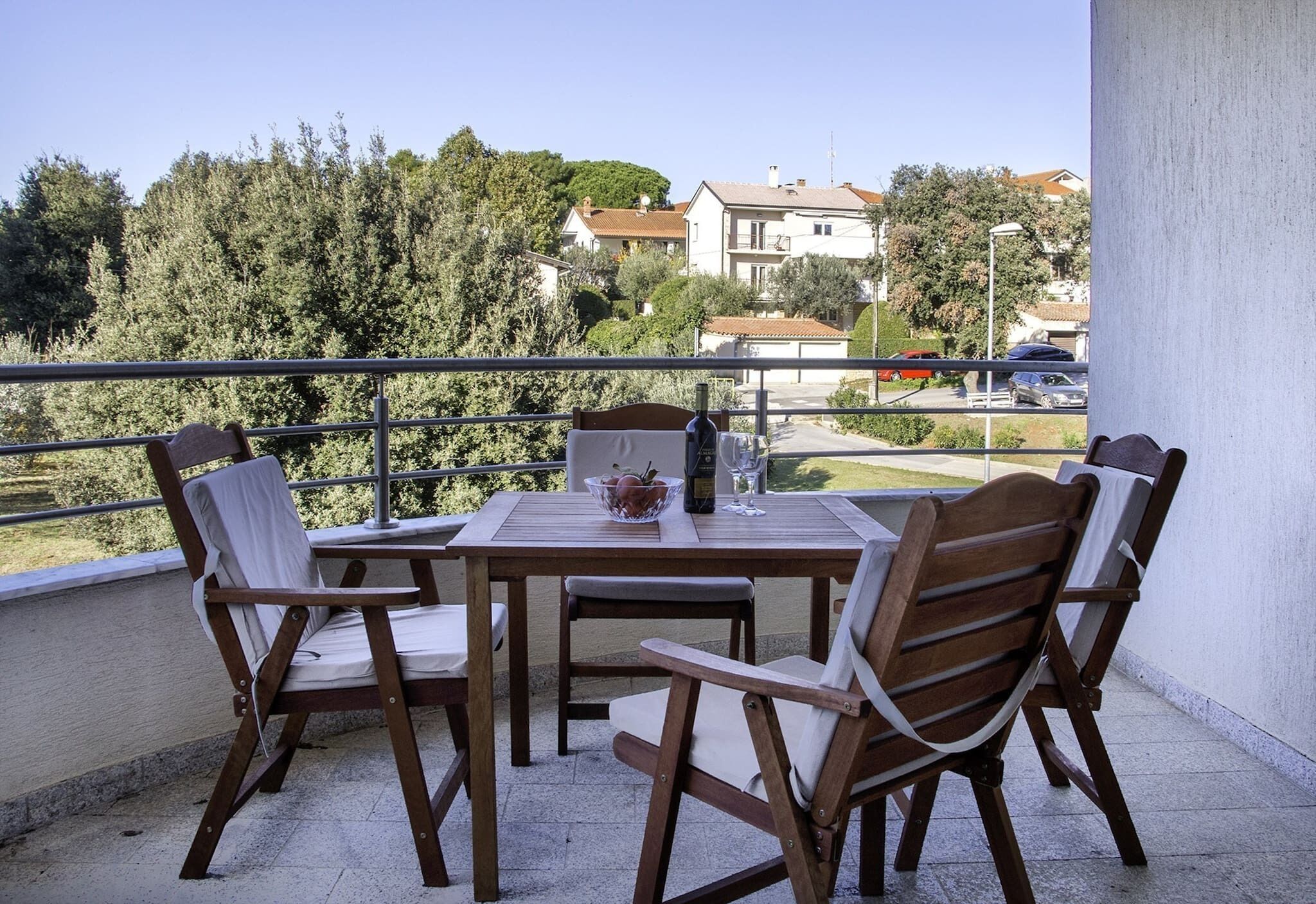 Un balcon avec une table et des chaises en bois, un saladier et une bouteille.