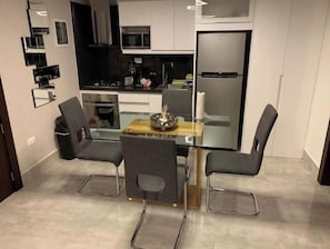 A modern kitchen with a dining table and chairs, a refrigerator, and a microwave.