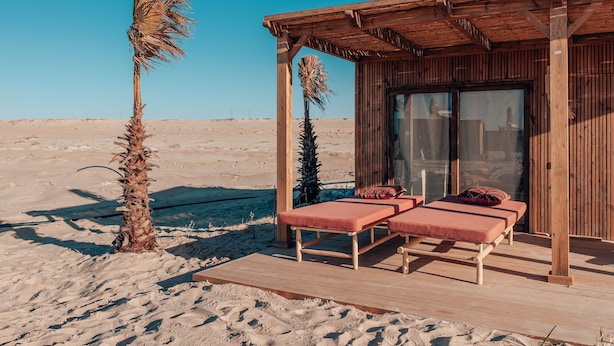 Estructura de madera con dos tumbonas y un ventanal, con un paisaje desértico de fondo.