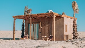 Una pequeña estructura de madera con techo de paja, dos sillas y una palmera.