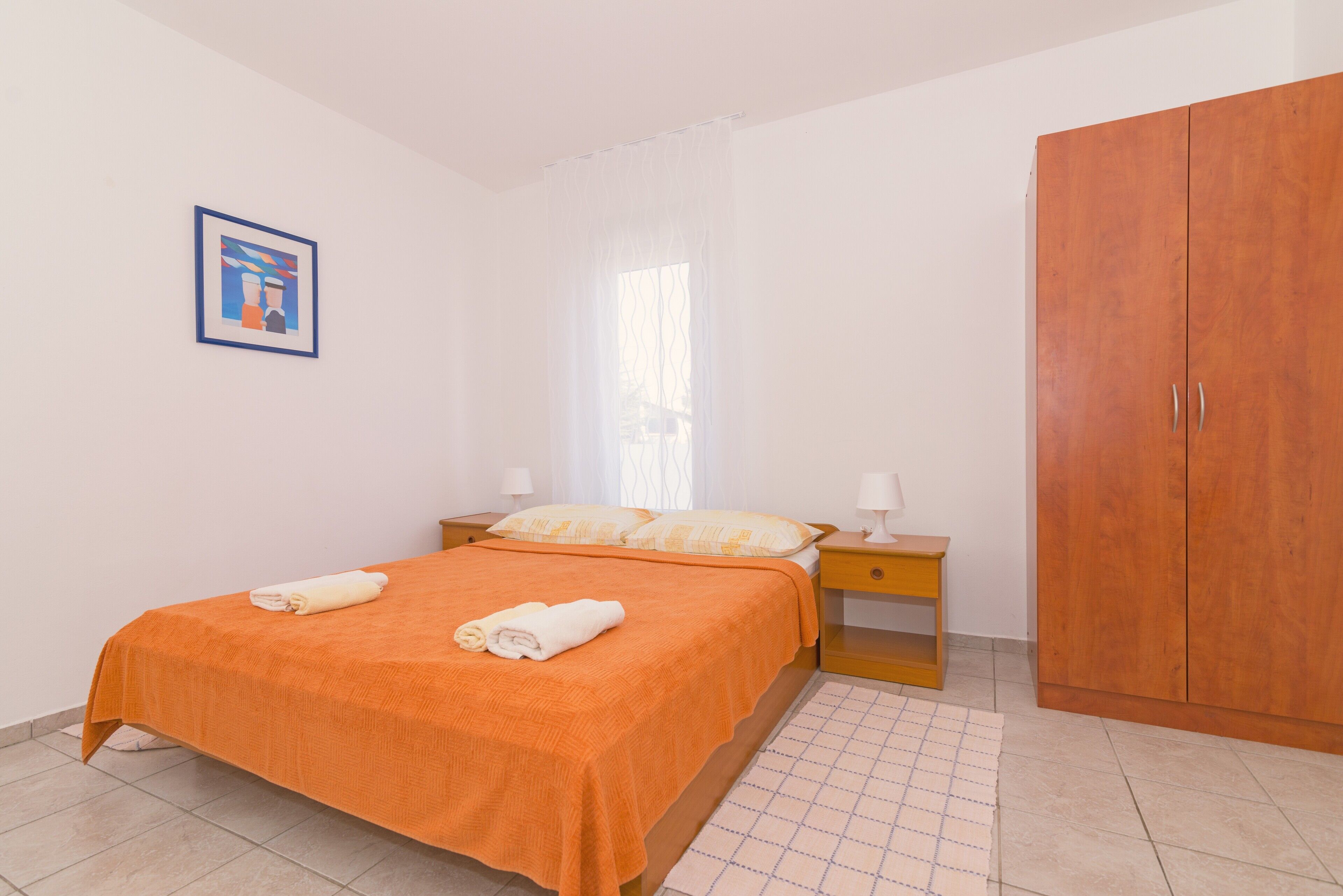 A bedroom with a bed, nightstands, a wardrobe, and a framed picture on the wall.