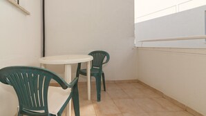 Ein kleiner Balkon mit einem runden Tisch und zwei grünen Stühlen.