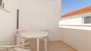 A small balcony with a white table and chairs, a window, and a tiled floor. - Studio apartment on the second floor (Pirovac)