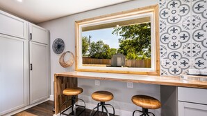 A kitchen with a wooden countertop, three bar stools, a large mirror, and a view of the backyard. - Unwind & Recharge in Style! Honey Bee Cottage is a Perfect Medical Ctr. Retreat! (San Antonio)