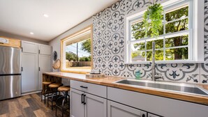 A modern kitchen with white cabinetry, a wooden countertop, and a large window with a view of trees. - Unwind & Recharge in Style! Honey Bee Cottage is a Perfect Medical Ctr. Retreat! (San Antonio)