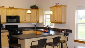 A kitchen with wooden cabinets, a black microwave, a stove, and a large island with bar stools.