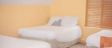A room with two single beds, beige walls, and a window with blinds.