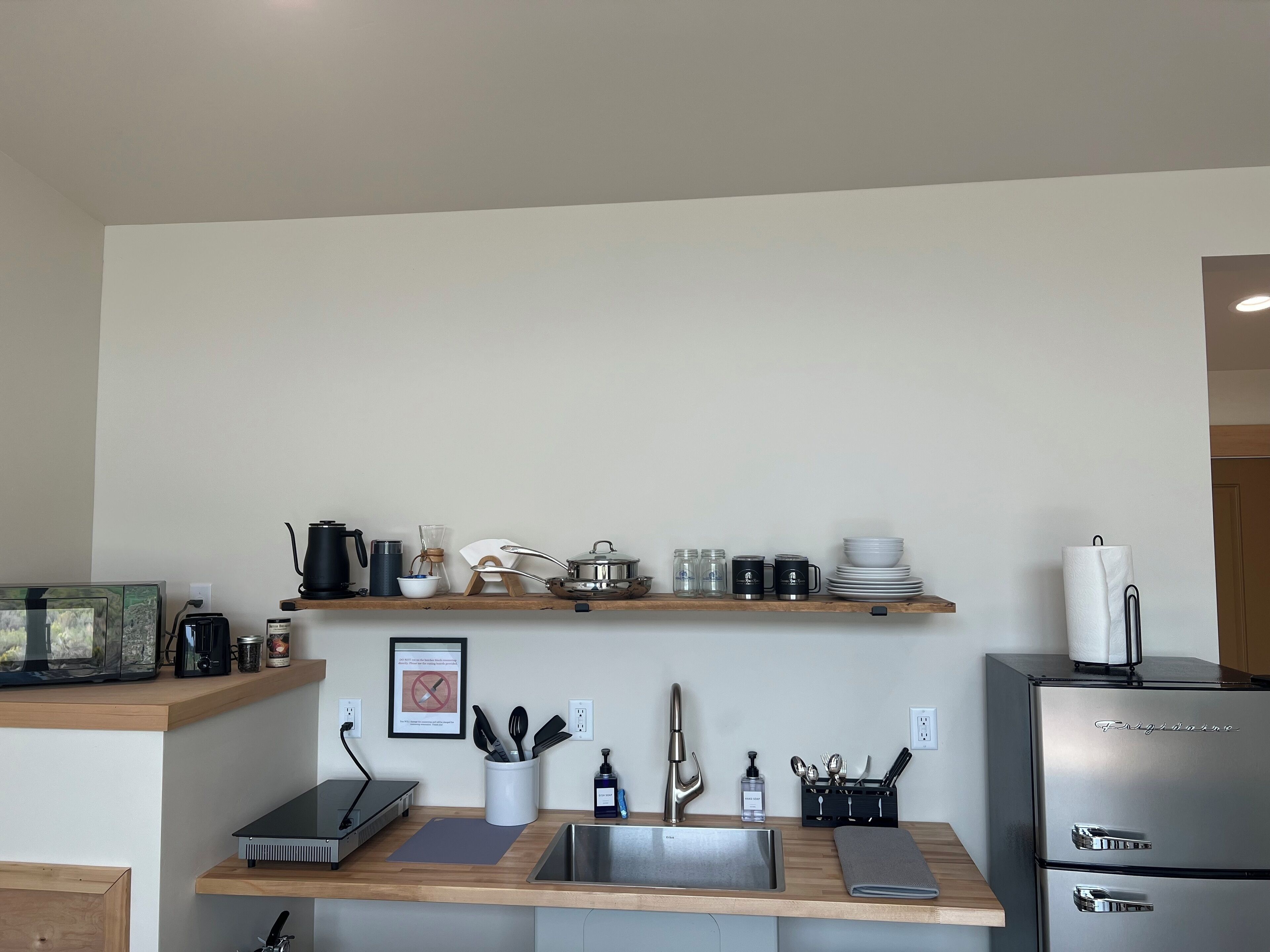 A modern kitchen with a built-in sink, wooden shelves, and a refrigerator.