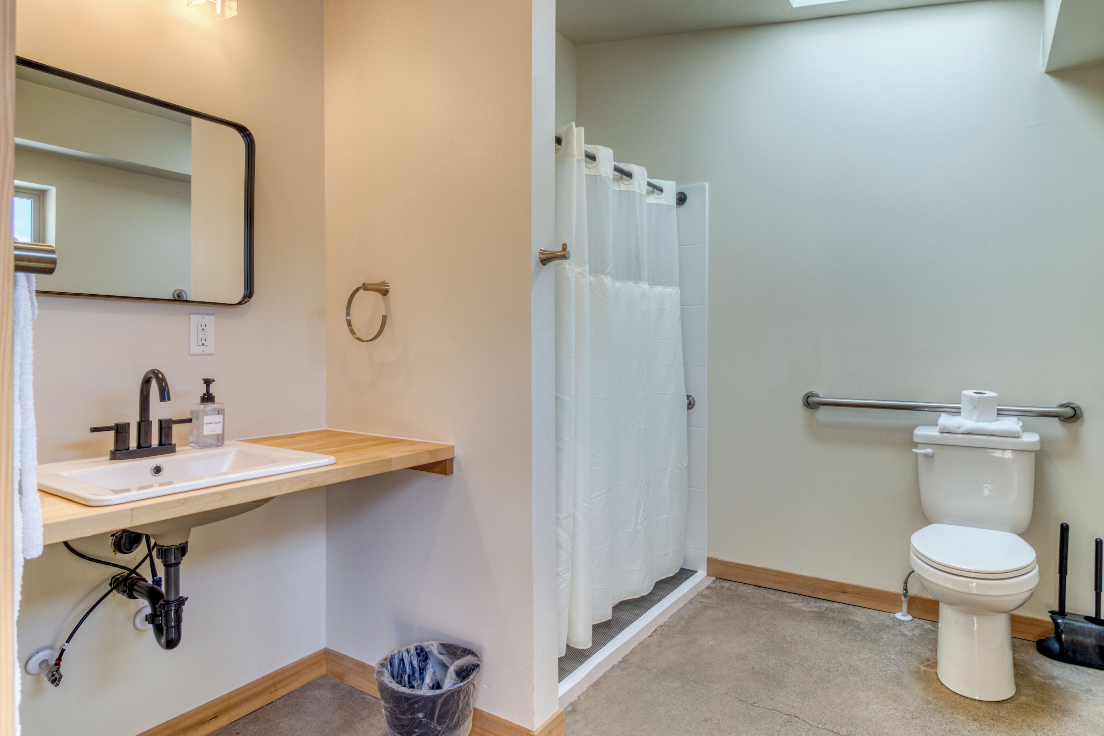 A bathroom with a sink, mirror, toilet, shower curtain, and a grab bar.