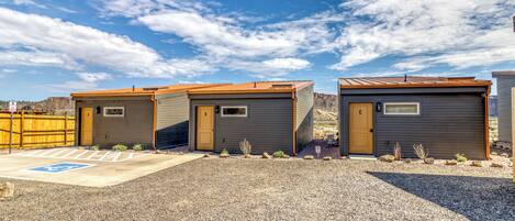 Een rij kleine, gelijkvloerse hutten met een grindpad en een parkeerplaats voor mindervaliden.