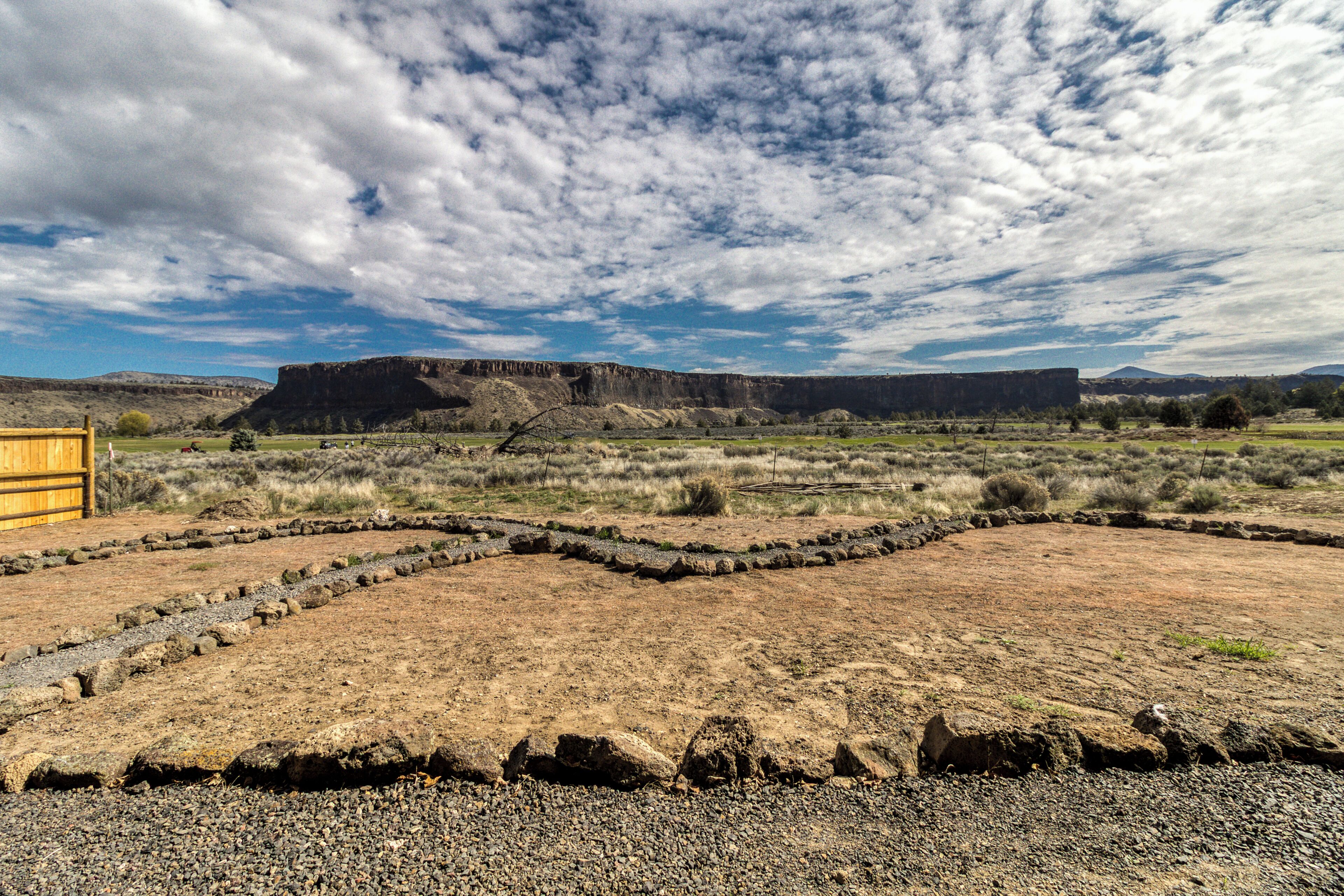 A dry, rocky landscape with a wooden structure and a large rock formation in the distance.