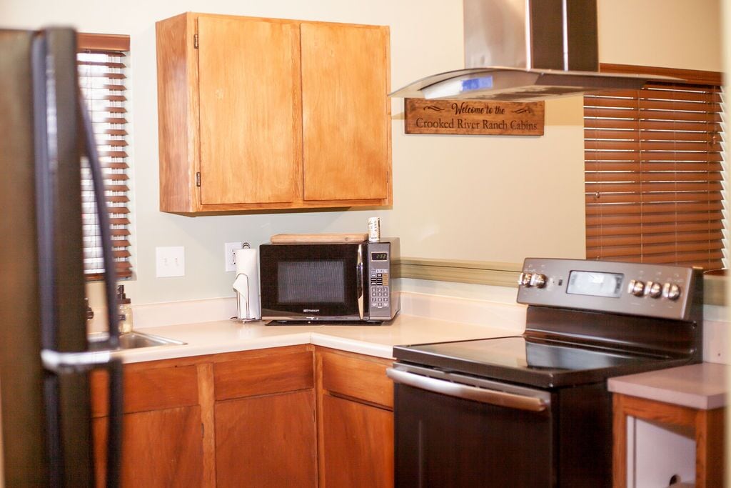 Una cocina con armarios de madera, microondas, horno y extractor de acero inoxidable.