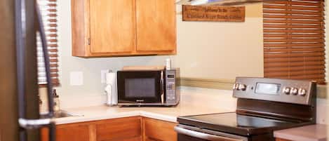 Una cocina con armarios de madera, microondas, horno y extractor de acero inoxidable.