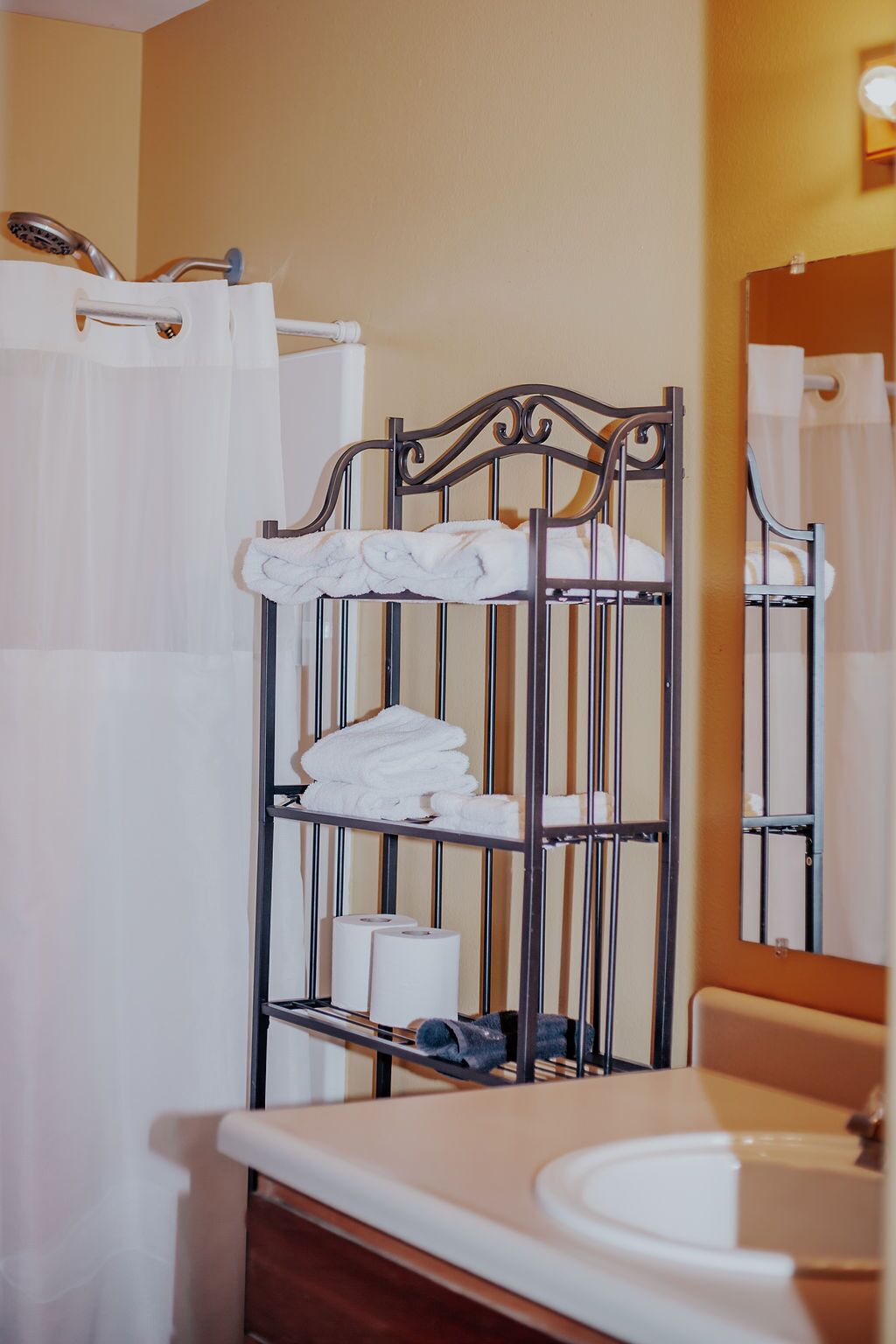 A bathroom with a metal towel rack holding white towels, a sink, and a mirror.