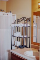 Un baño con un toallero metálico que sostiene toallas blancas, un lavamanos y un espejo.