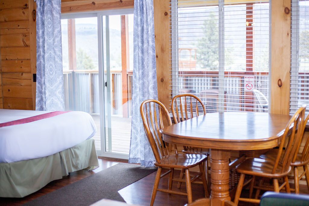 Een houten kamer met een bed, een eettafel met stoelen, en een balkon met uitzicht.