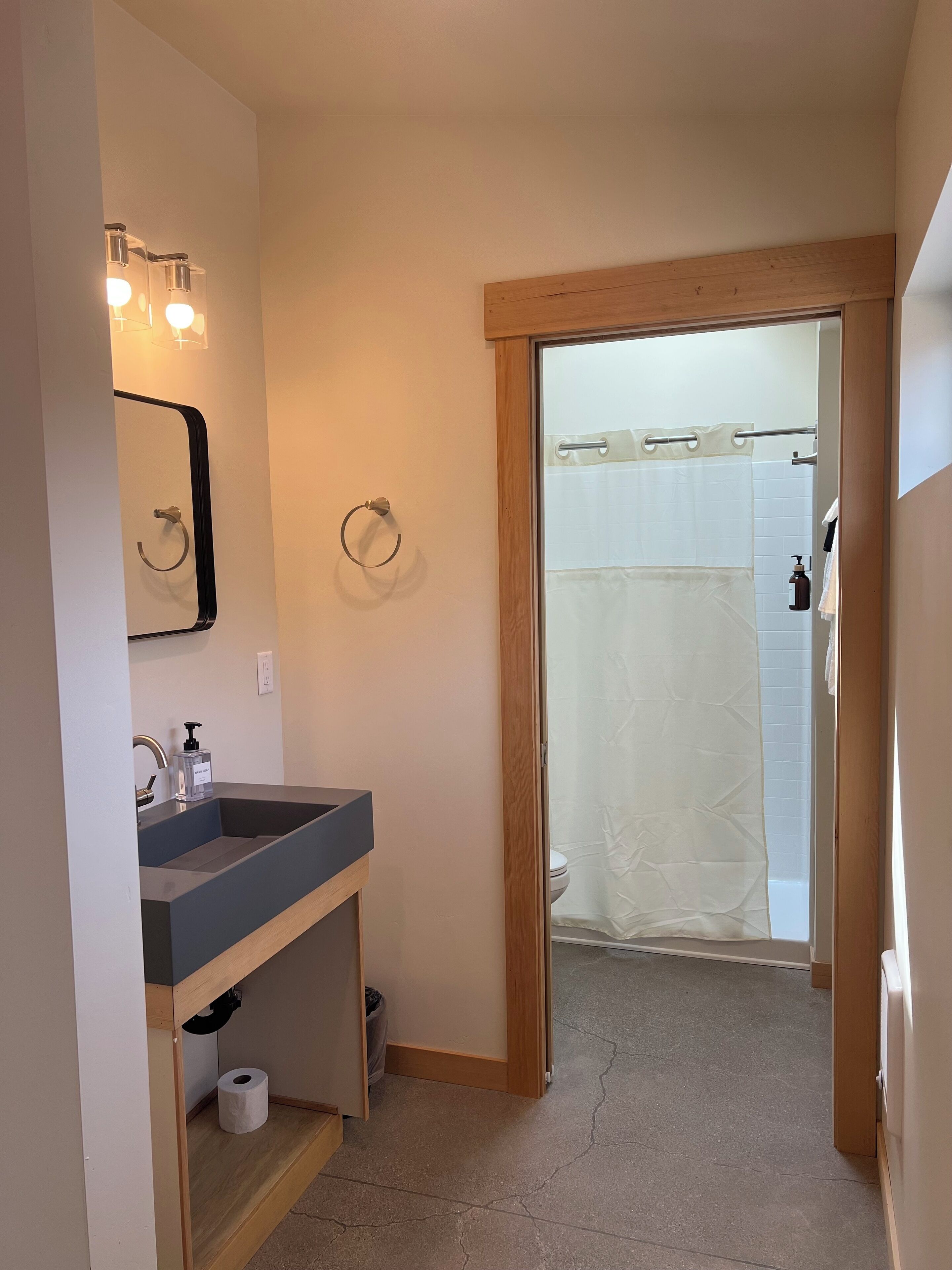 A bathroom with a sink, mirror, towel rings, and a shower area.