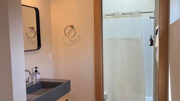 A bathroom with a sink, mirror, towel rings, and a shower area.