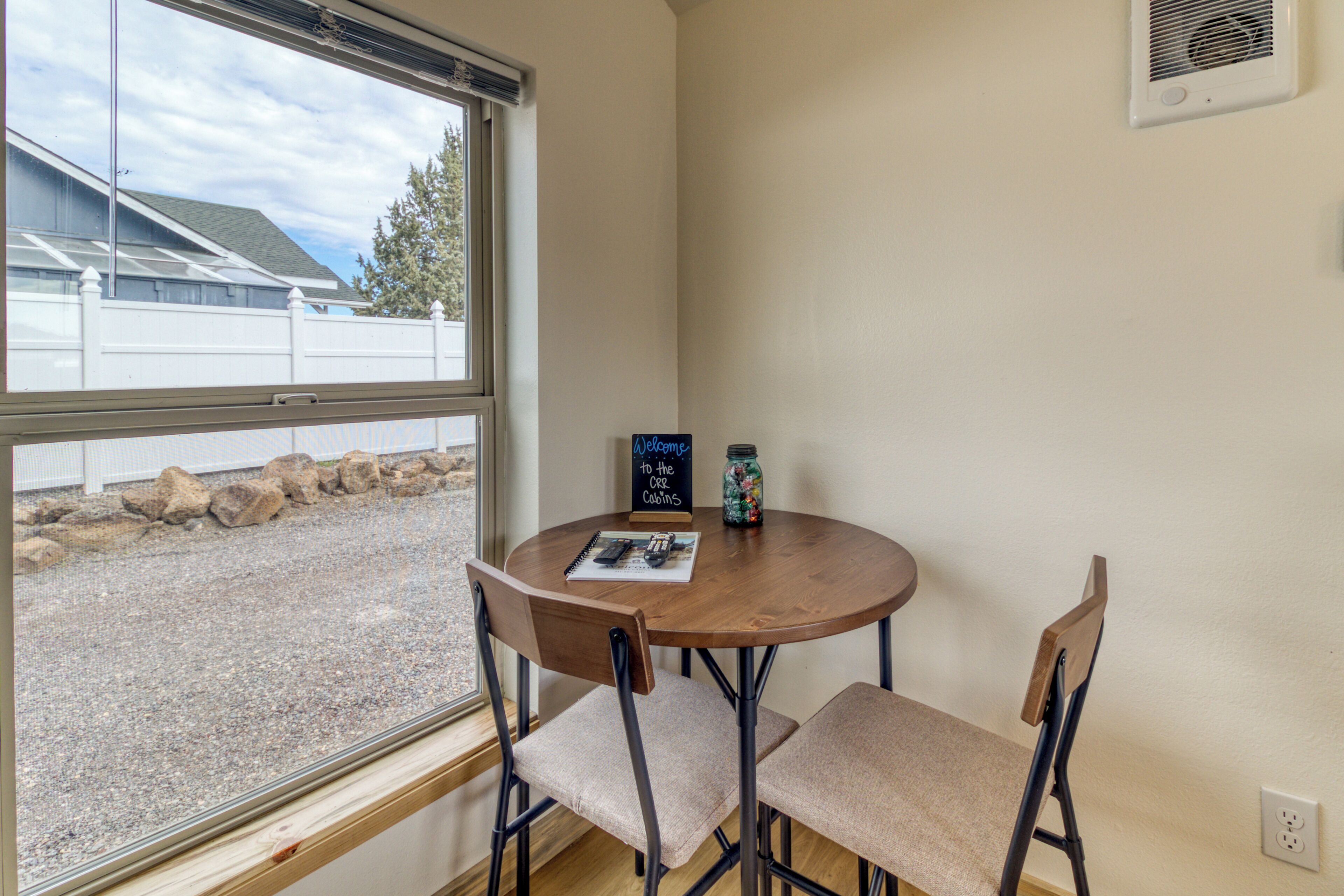 A corner room with a round table, two chairs, a window, and a 'Welcome to the Carlin's' sign.