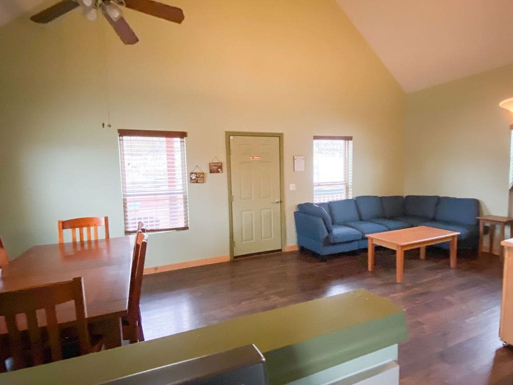 A living room with a dining table, blue sofa, and a ceiling fan.