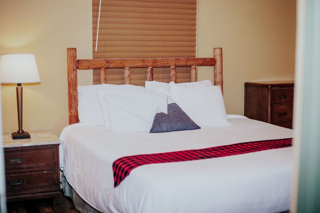 A neatly made bed with white linens and a red and black checkered throw blanket.